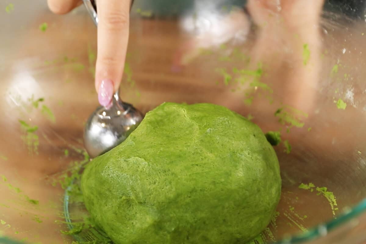 scooping matcha sugar cookie dough from glass bowl