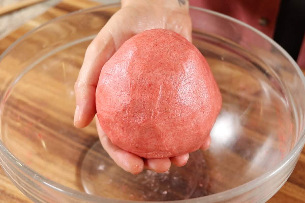 hand holding a ball of strawberry sugar cookie dough