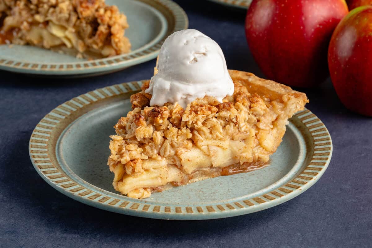 slice of apple crumble pie with ice cream on top and apples peaking in from the side