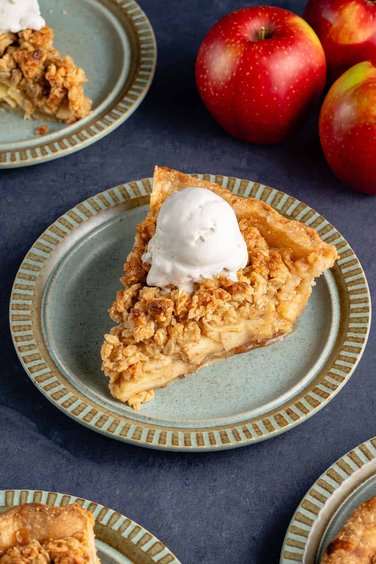 slice of apple crumble pie with ice cream on top and apples peaking in from the side