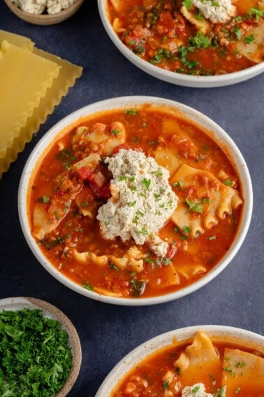 bowls of lasagna soup topped with ricotta and parsley