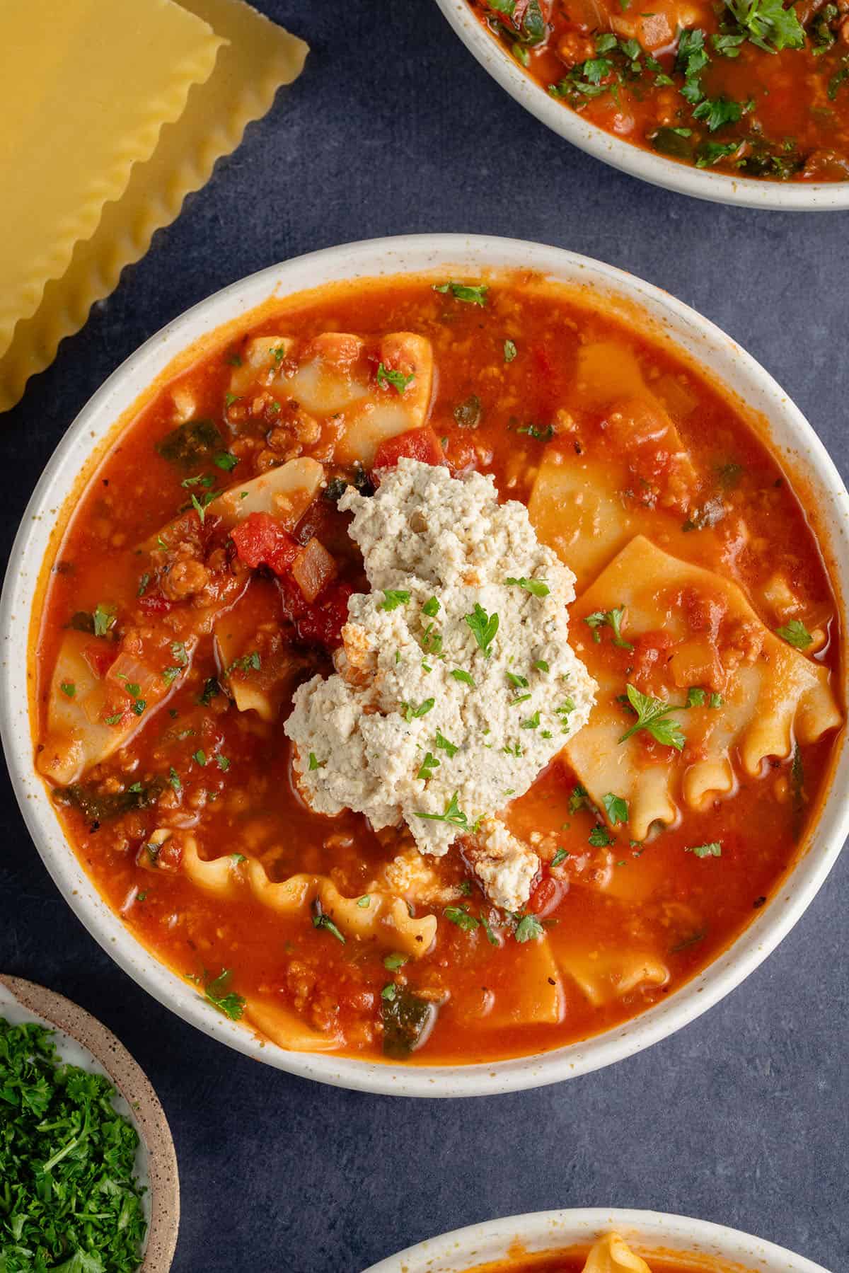 bowls of lasagna soup topped with ricotta and parsley
