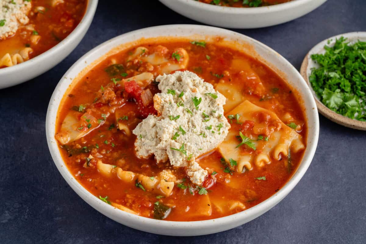 bowls of lasagna soup topped with ricotta and parsley