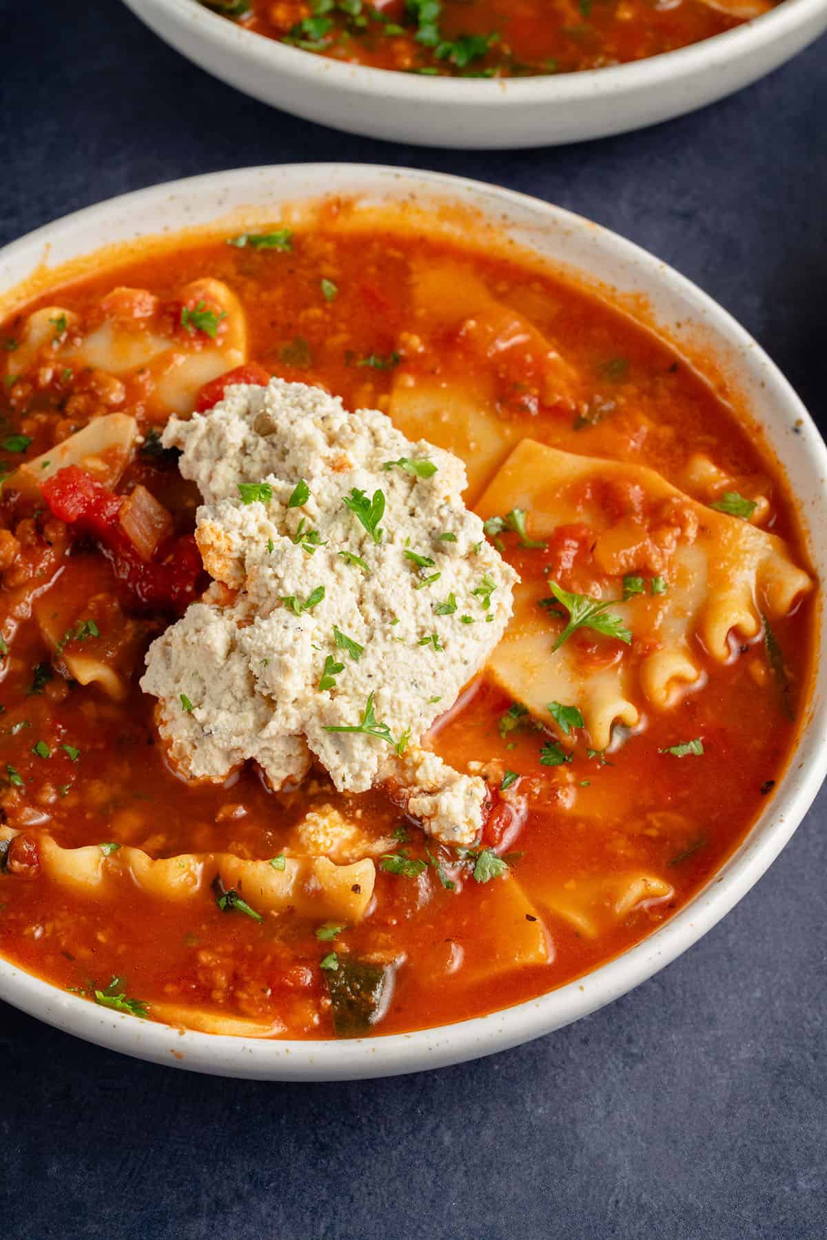 bowls of lasagna soup topped with ricotta and parsley