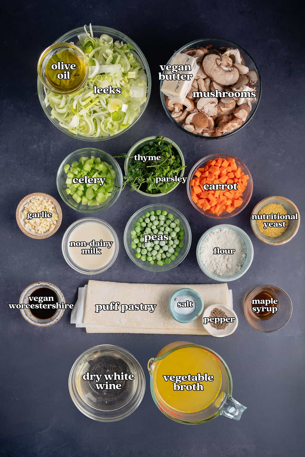labelled ingredients for Vegan Mushroom Pot Pie: olive oil, leeks, vegan butter, mushrooms, celery, thyme, parsley, carrot, garlic, non-dairy milk, peas, flour, nutritional yeast, vegan Worcestershire, puff pastry, salt, pepper, maple syrup, dry white wine and vegetable broth