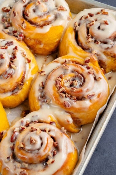 fluffy pumpkin cinnamon rolls with icing and pecans on a baking sheet