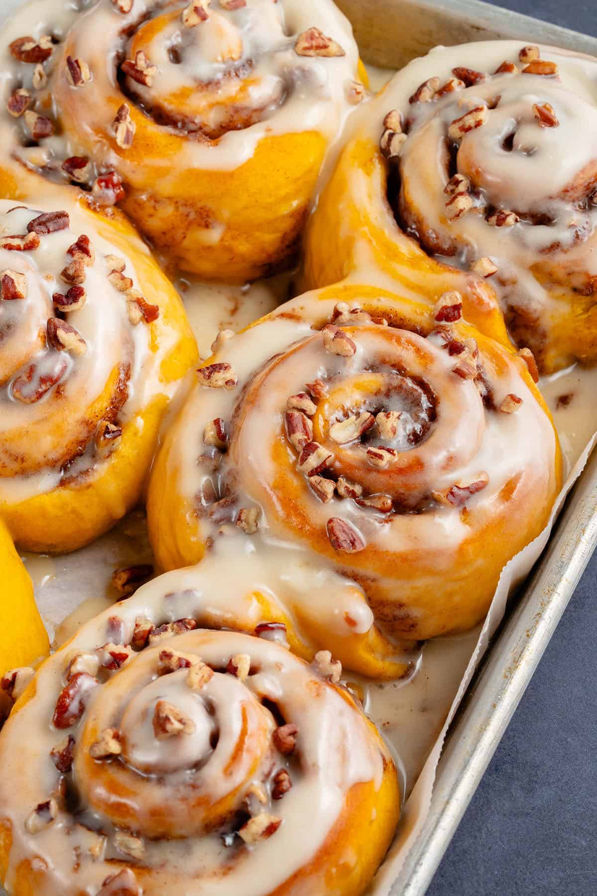 fluffy pumpkin cinnamon rolls with icing and pecans on a baking sheet
