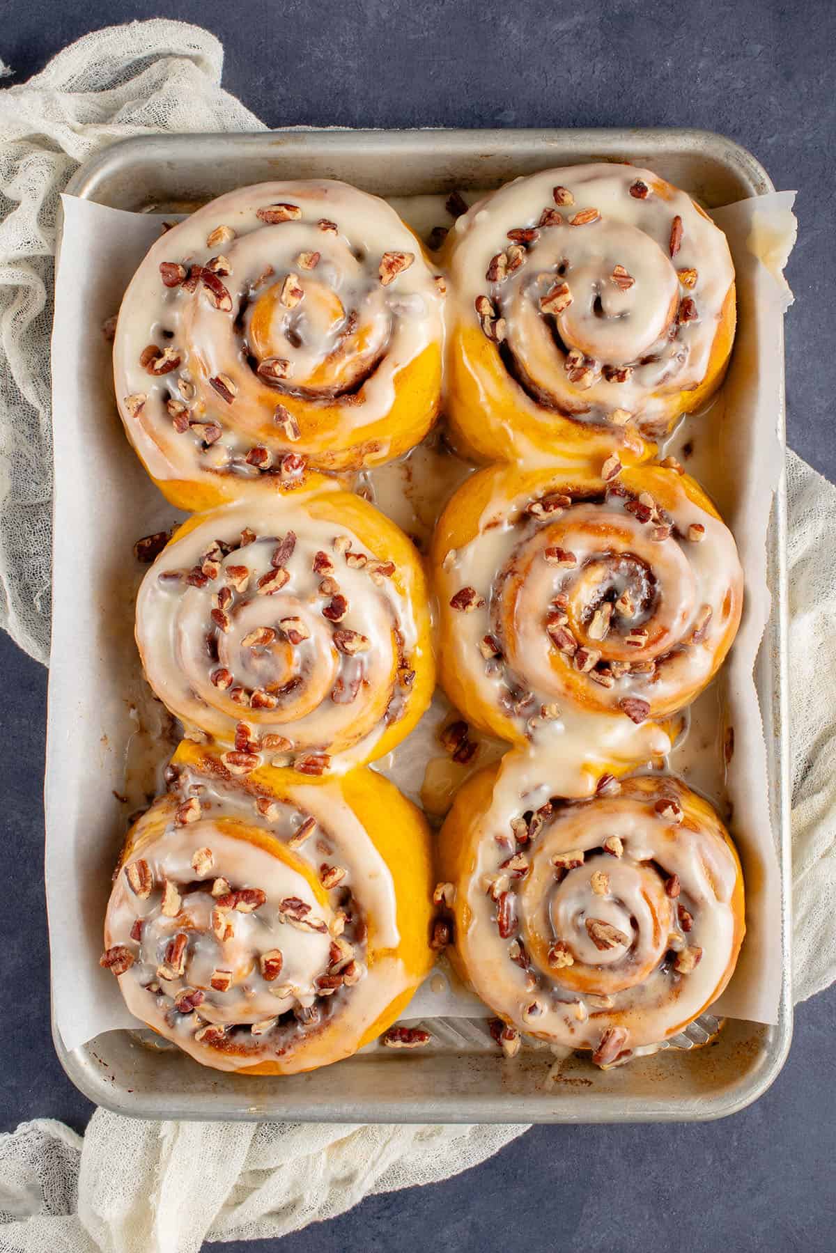 fluffy pumpkin cinnamon rolls with icing and pecans on a baking sheet