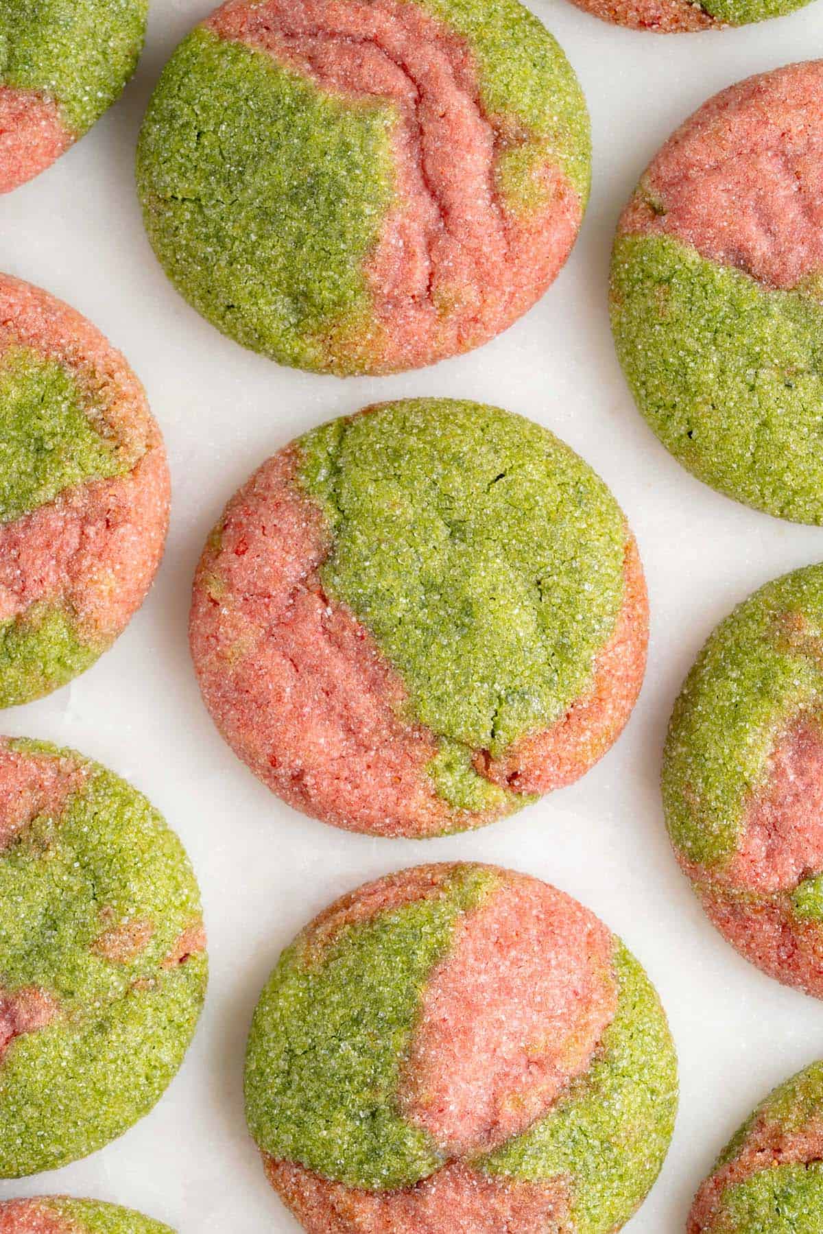 overhead photo of marbled pink and green cookies on a white marble board