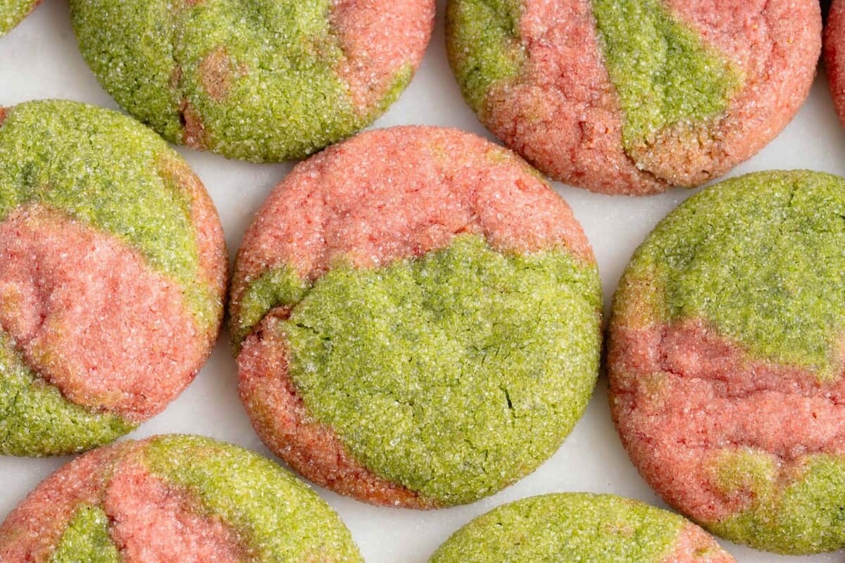 horizontal photo of marbled pink and green cookies on a white marble board