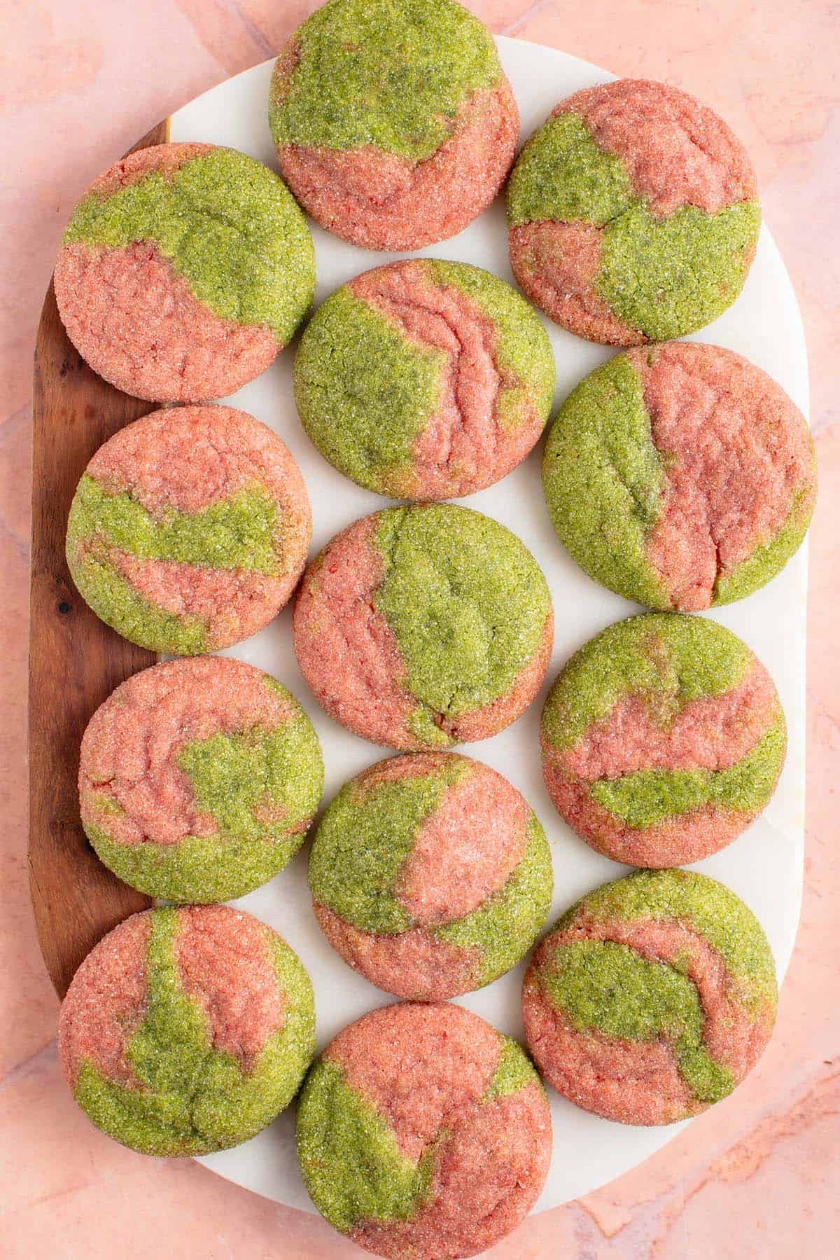 overhead photo of marbled pink and green cookies on a white marble board