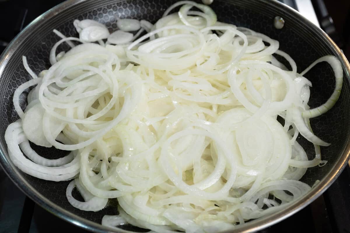 thinly sliced onions in large black pan