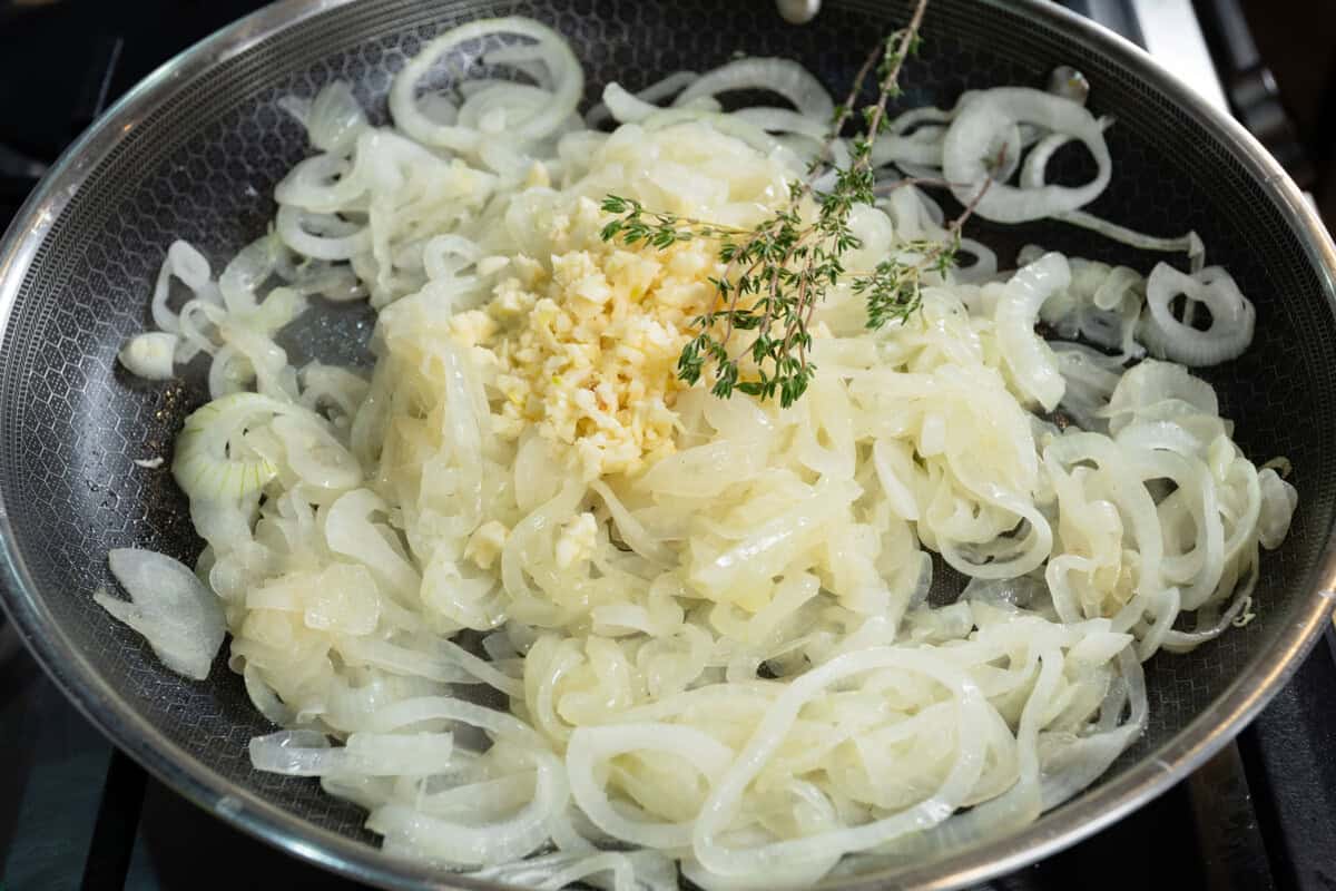 cooking thinly sliced onions in large black pan with garlic and thyme