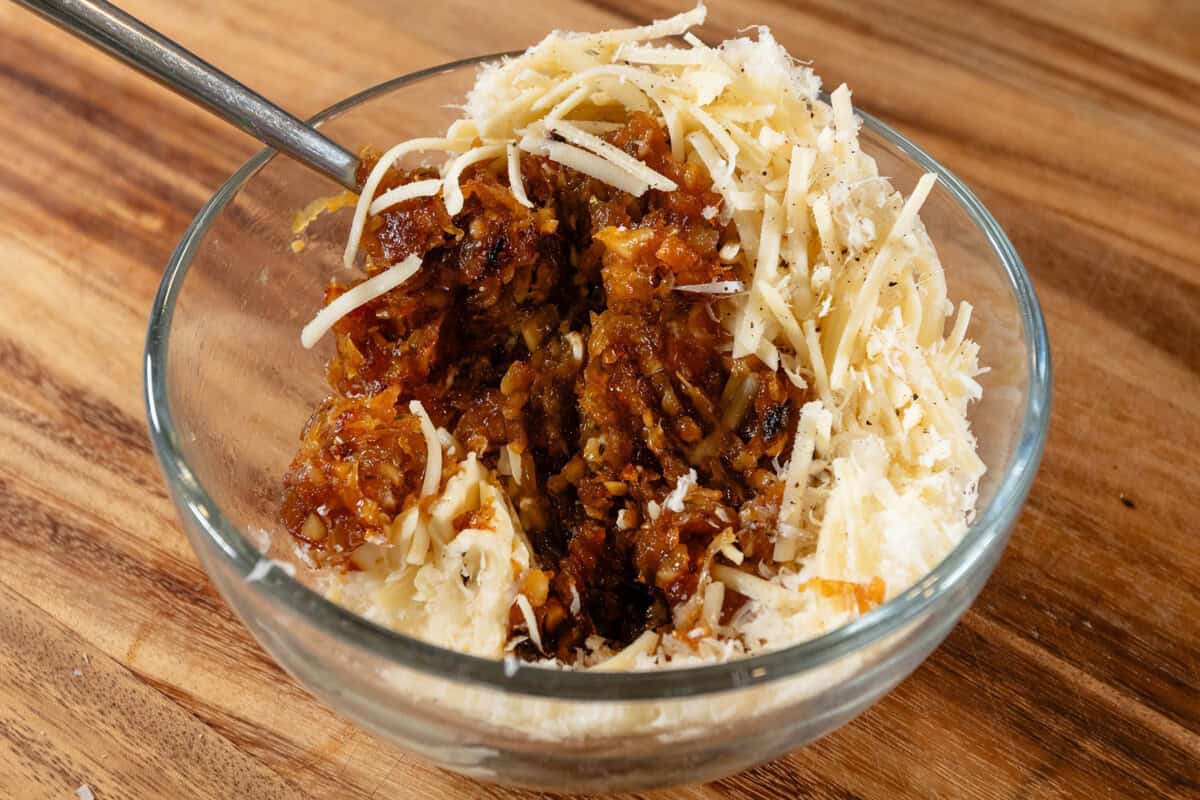 mixing caramelized onions with butter and cheese in glass bowl