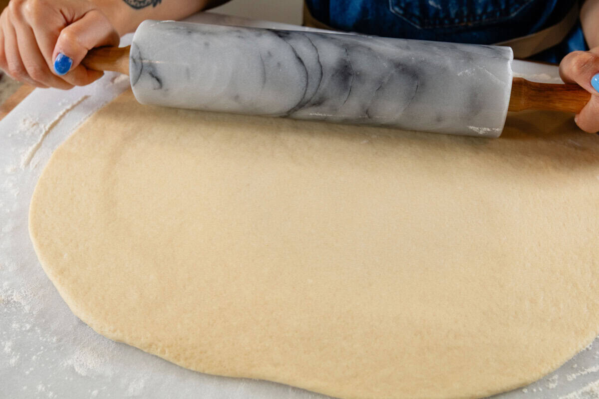 rolling out bread dough with a marble rolling pin on white surface