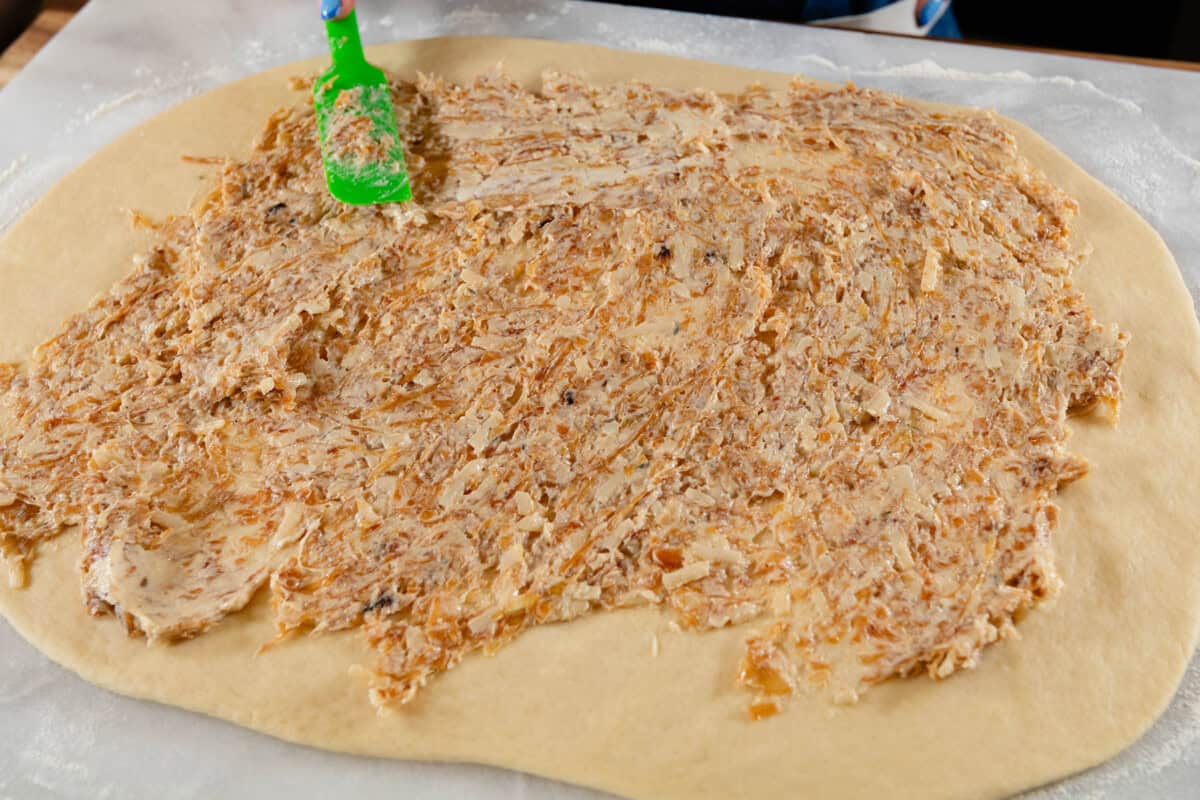 spreading caramelized onion butter onto flattened dough