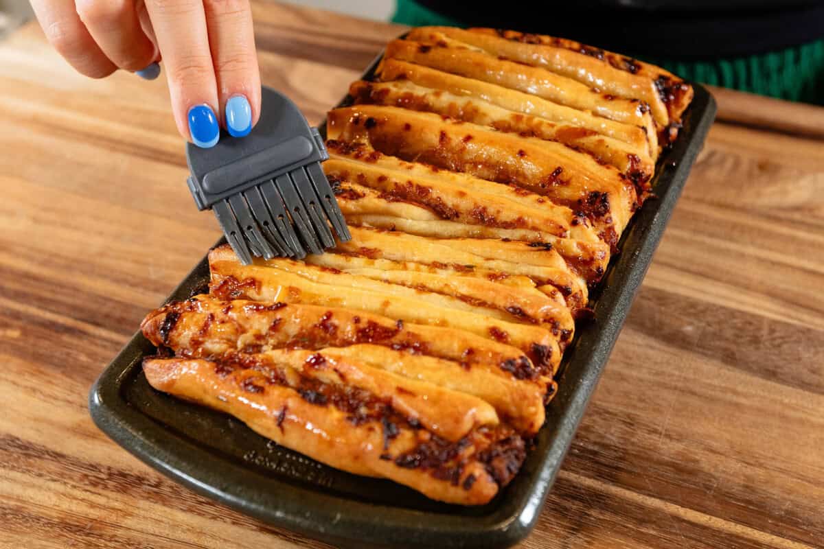 brushing melted butter onto french onion pull-apart bread in loaf pan