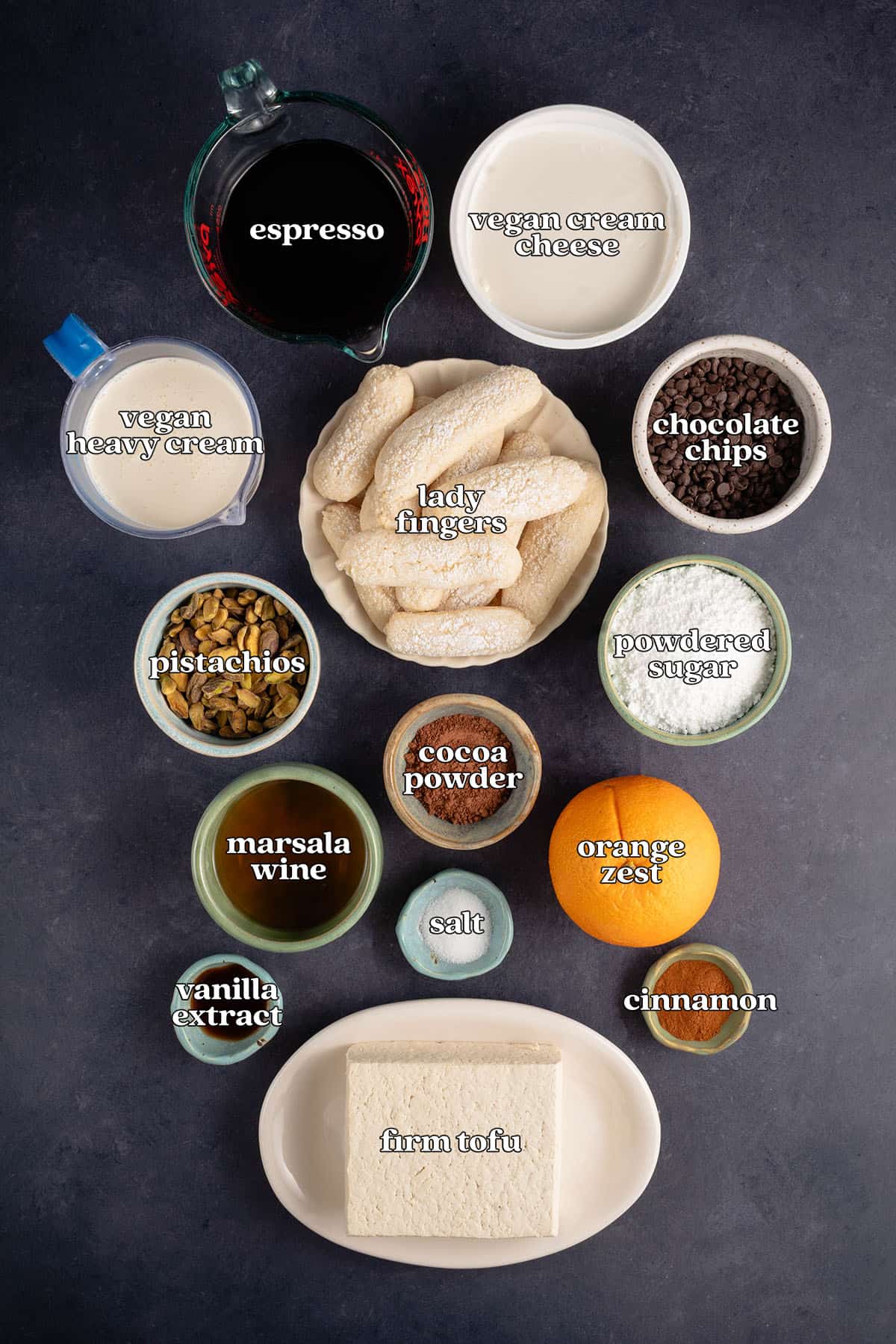 labeled ingredients for vegan cannoli tiramisu: espresso. vegan cream cheese. vegan heavy cream, lady fingers, chocolate chips, pistachios, powdered sugar, marsala wine, cocoa powder, orange zest, salt, vanilla extract, cinnamon, and firm tofu