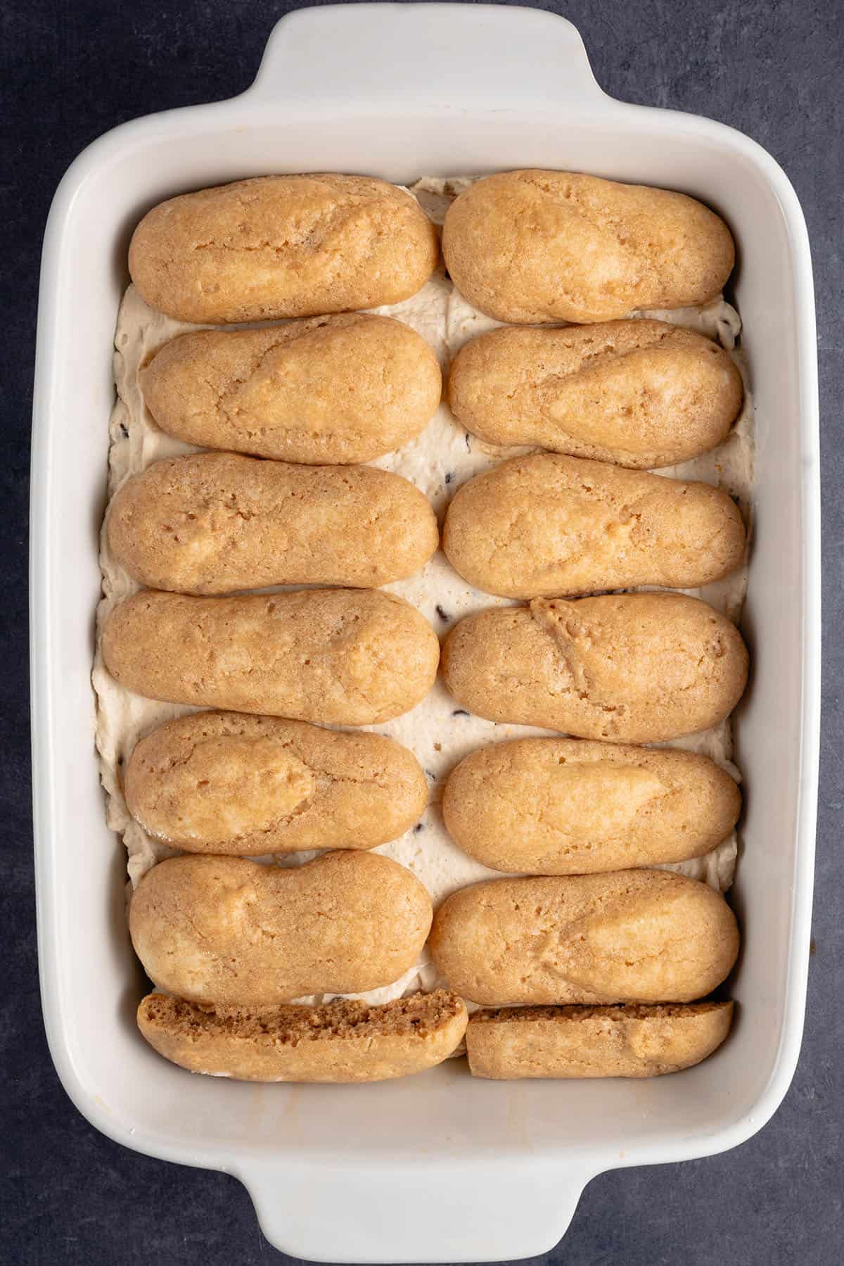 a layer of espresso soaked lady fingers on top of cannoli cream in a baking dish