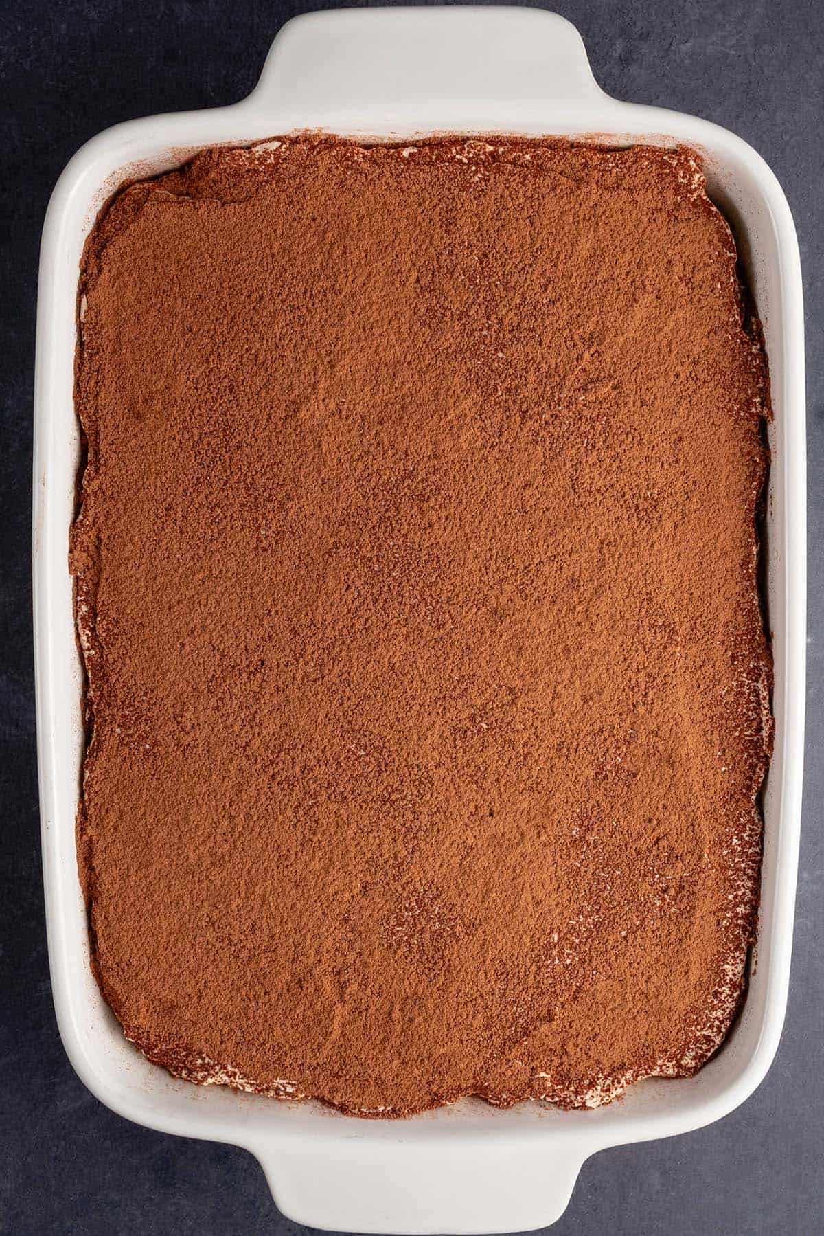 a tray of vegan cannoli tiramisu after being dusted with cocoa powder