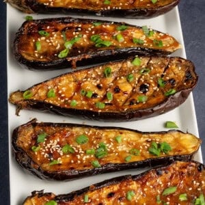 roasted miso-glazed eggplant on white serving plate with sesame seeds and green onion