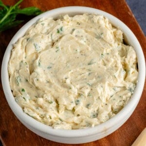 bowl of garlic butter on wooden platter with cloves of garlic and parsley