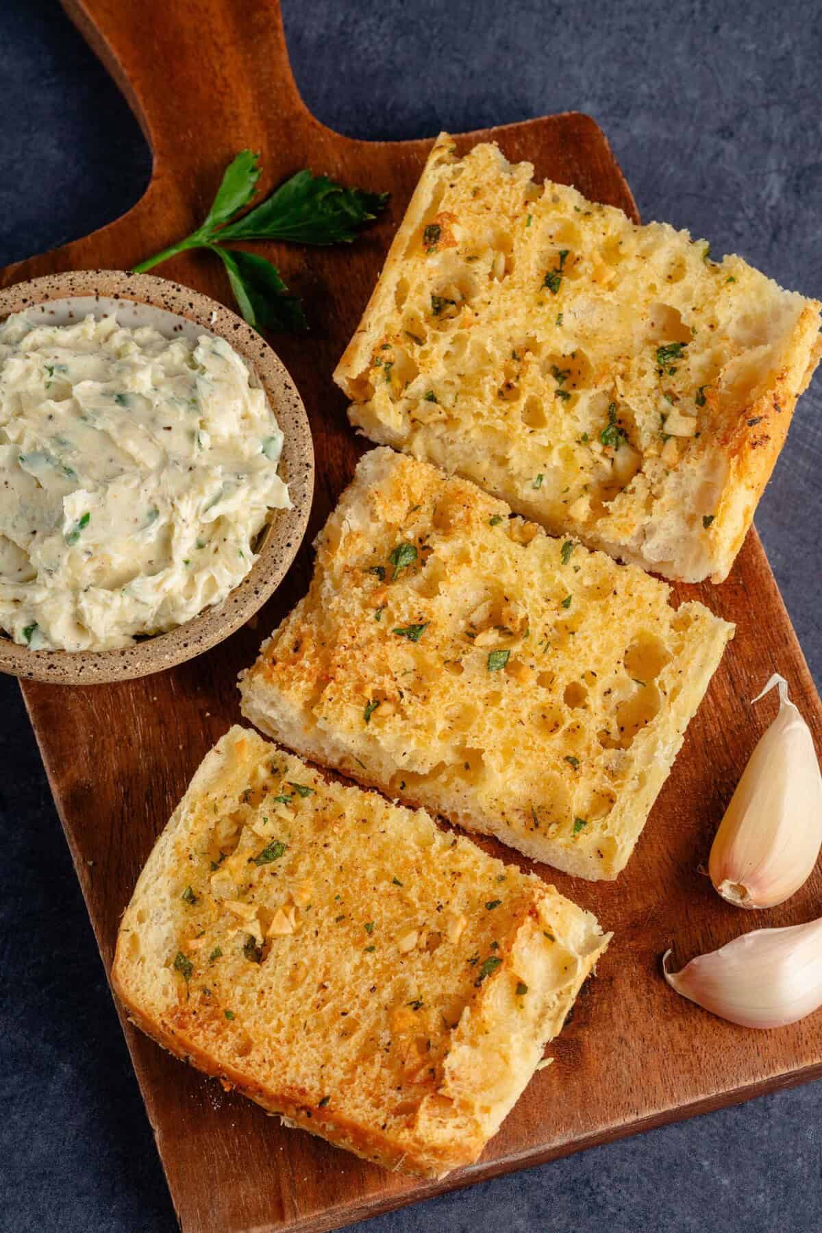 garlic bread on platter next to cup of garlic butter