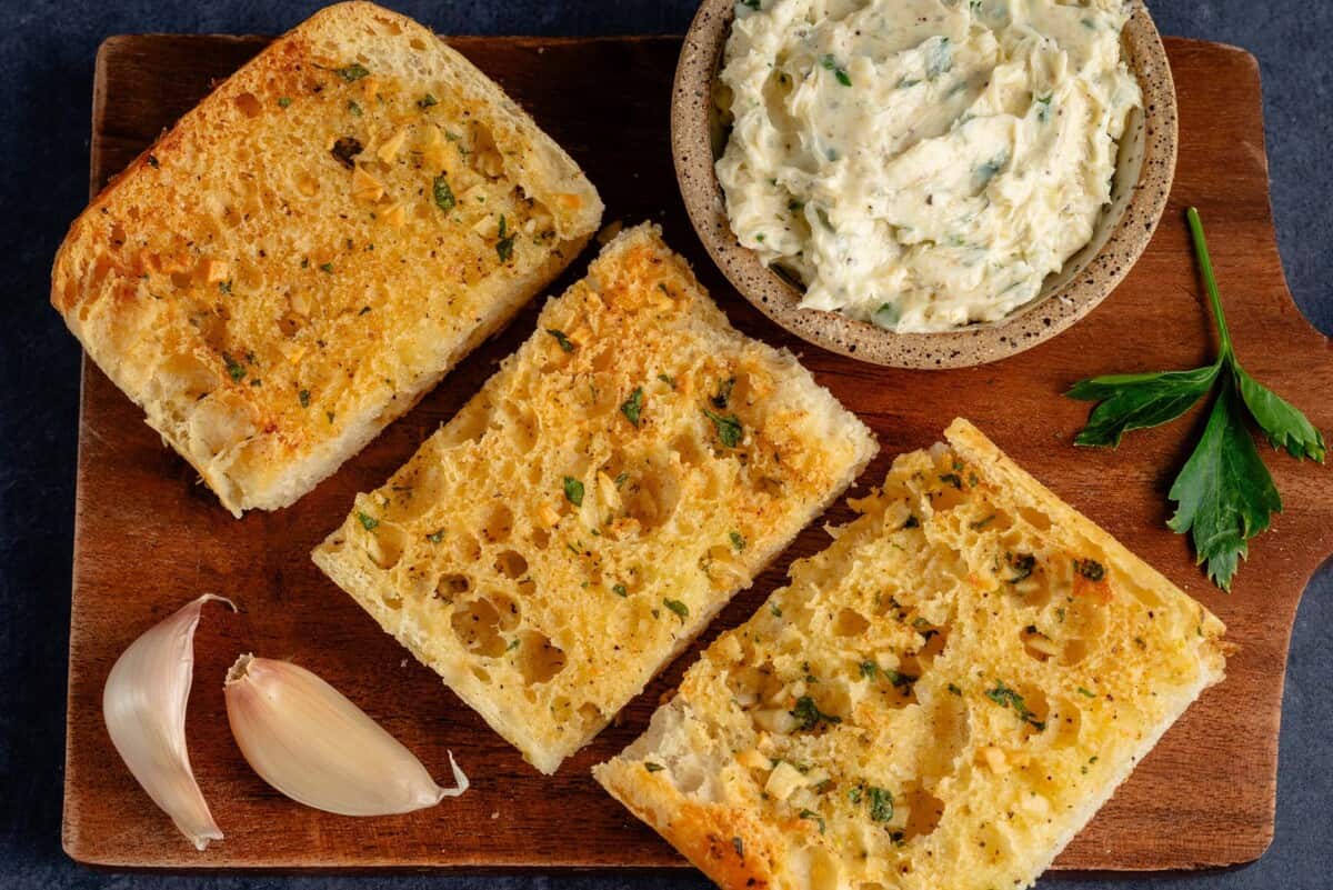 garlic bread on platter next to cup of garlic butter