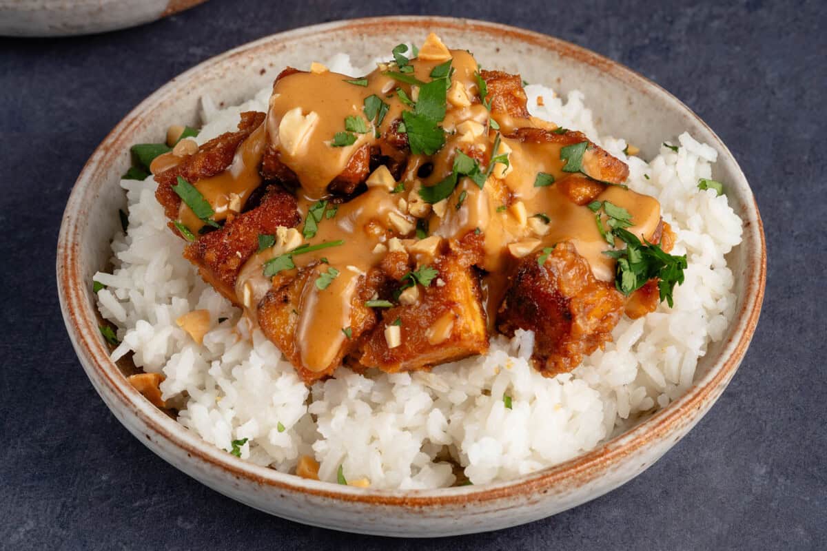 horizontal photo of a small bowl of white rice topped with easy peanut tofu with chopped peanuts and cilantro
