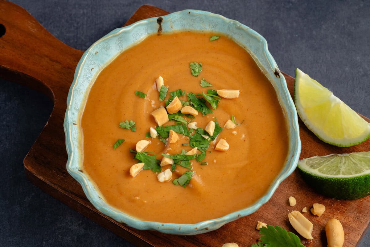 horizontal photo of peanut sauce topped with cilantro and roasted peanuts in blue speckled bowl