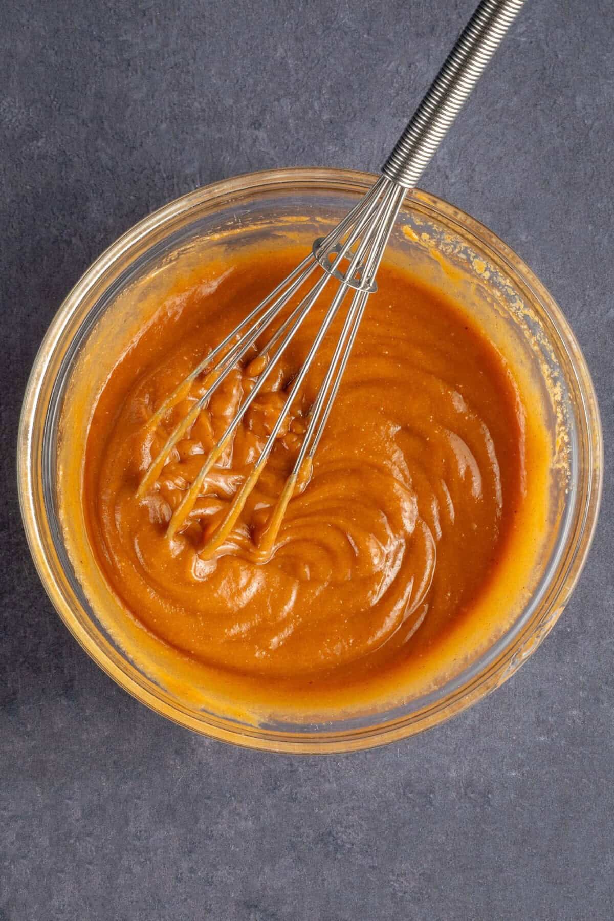 whisk with homemade peanut sauce in glass bowl