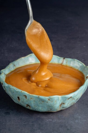 spoon overflowing with easy peanut sauce into blue speckled bowl