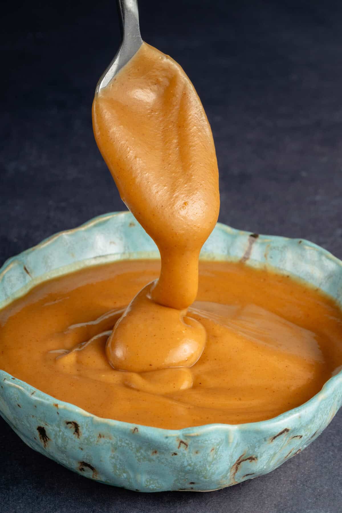 spoon overflowing with easy peanut sauce into blue speckled bowl