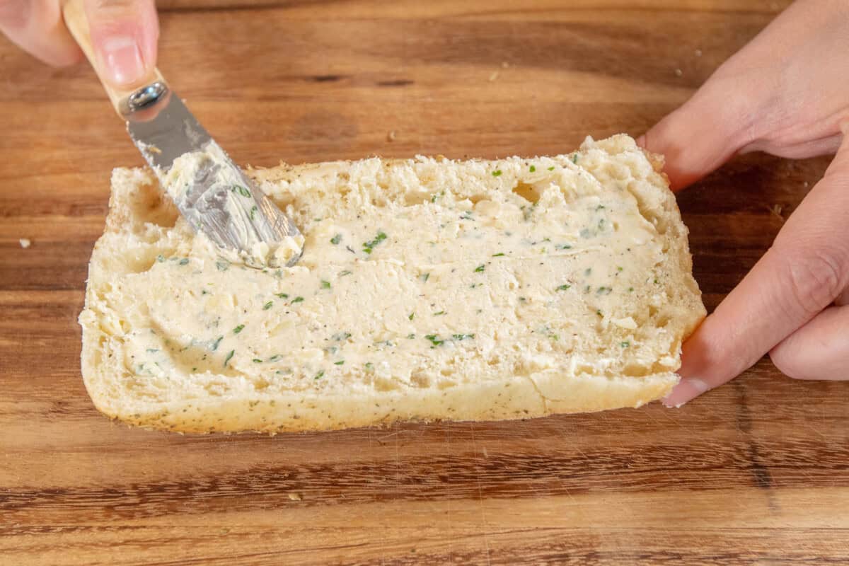 spreading garlic butter on garlic bread