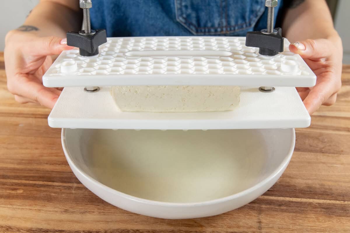 pressing tofu with liquid pouring into a bowl