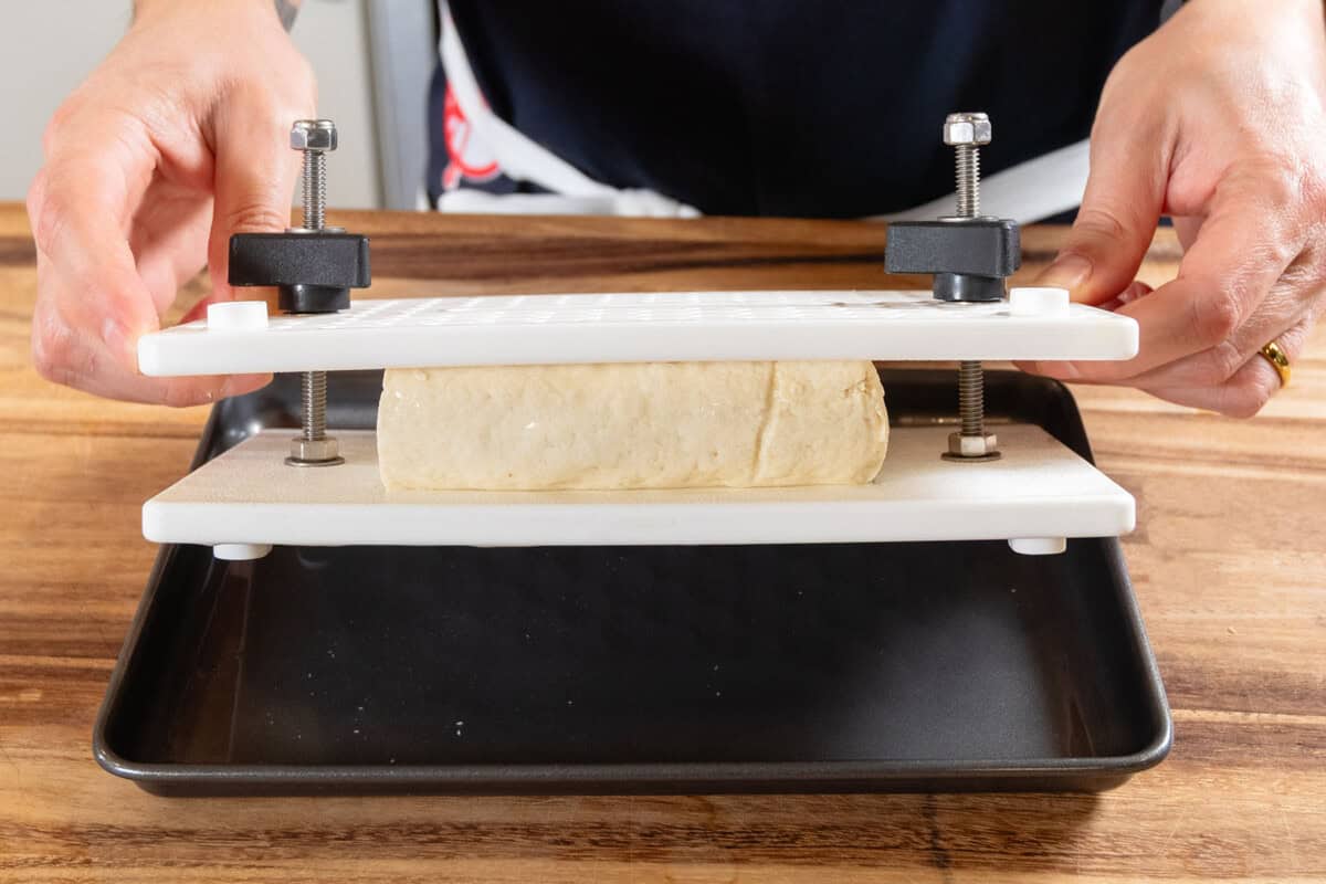 pressing a block of extra firm tofu with a white tofu press