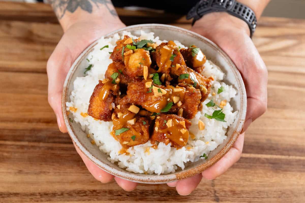 hands holding a small bowl with white rice and Easy peanut tofu topped with chopped peanuts and cilantro