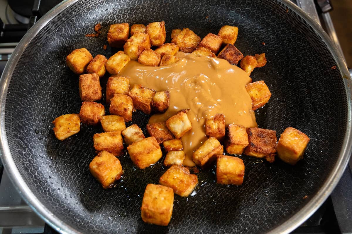 pan-fried cubes of extra firm tofu in large black hexclad pan with peanut sauce