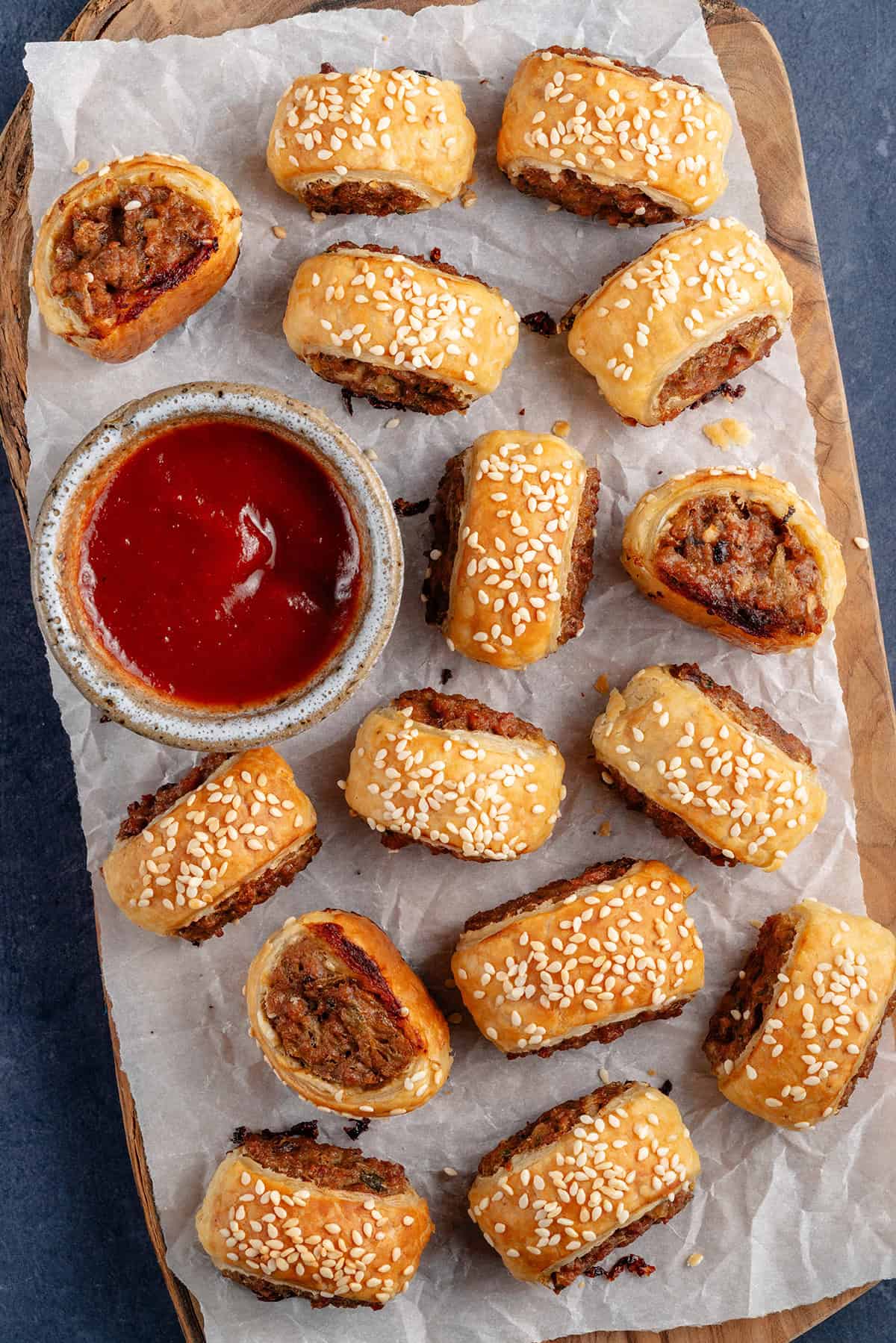 sausage rolls on a wooden board and parchment paper with a side of ketchup