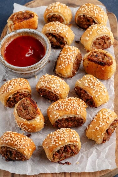 sausage rolls on a wooden board and parchment paper with a side of ketchup