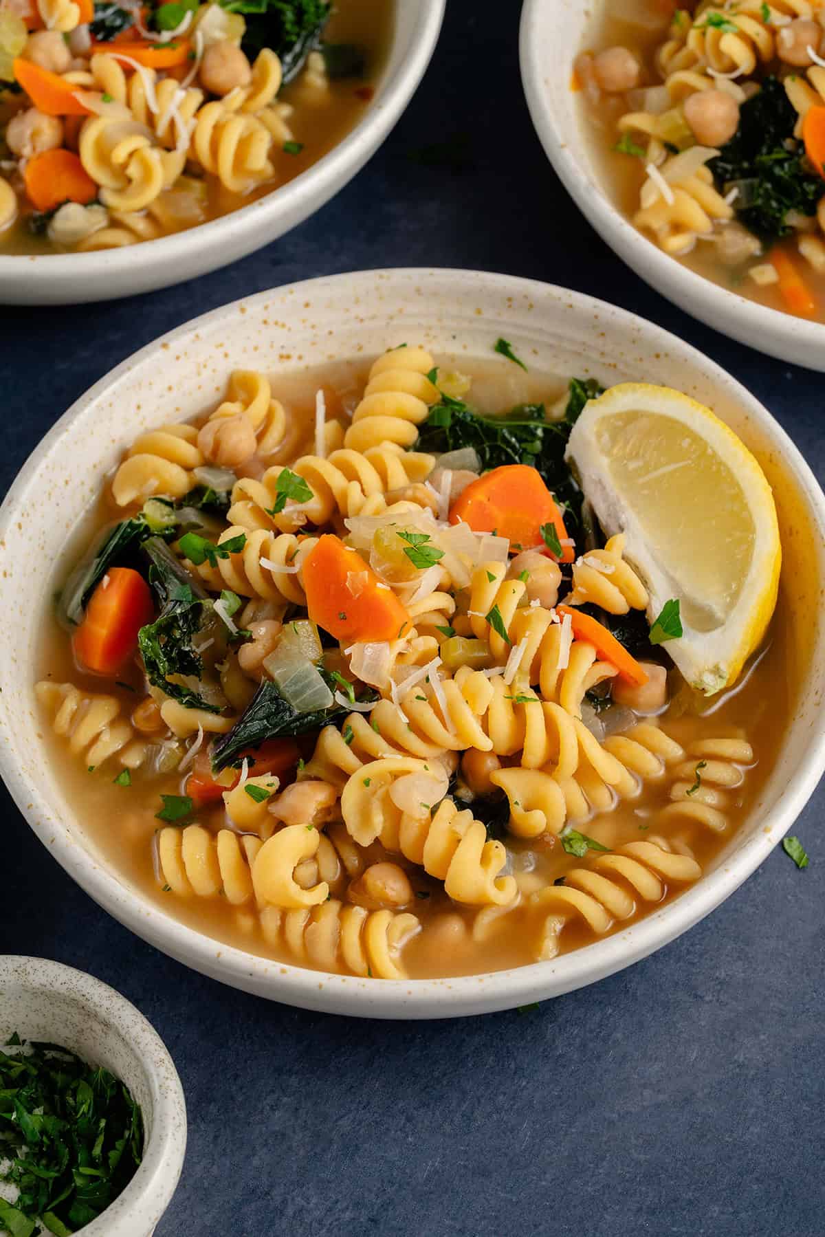 bowl of chickpea noodle soup with a lemon wedge surrounded by other bowls of soup