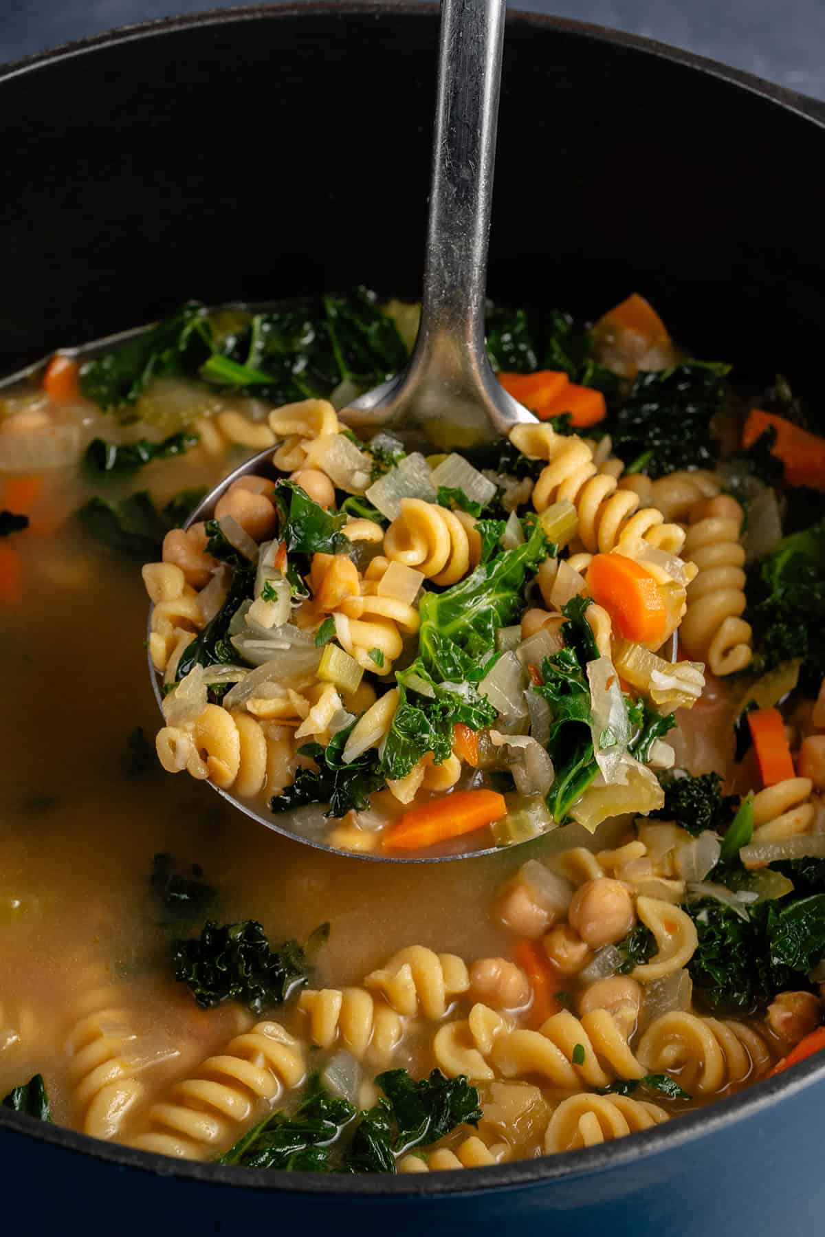 ladle full of chickpea noodle soup being scooped from pot