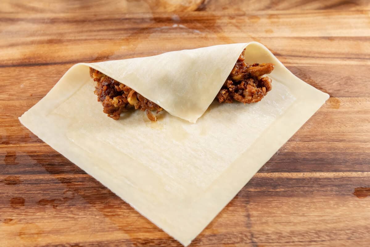 folding one corner of the egg roll wrapper over the filling