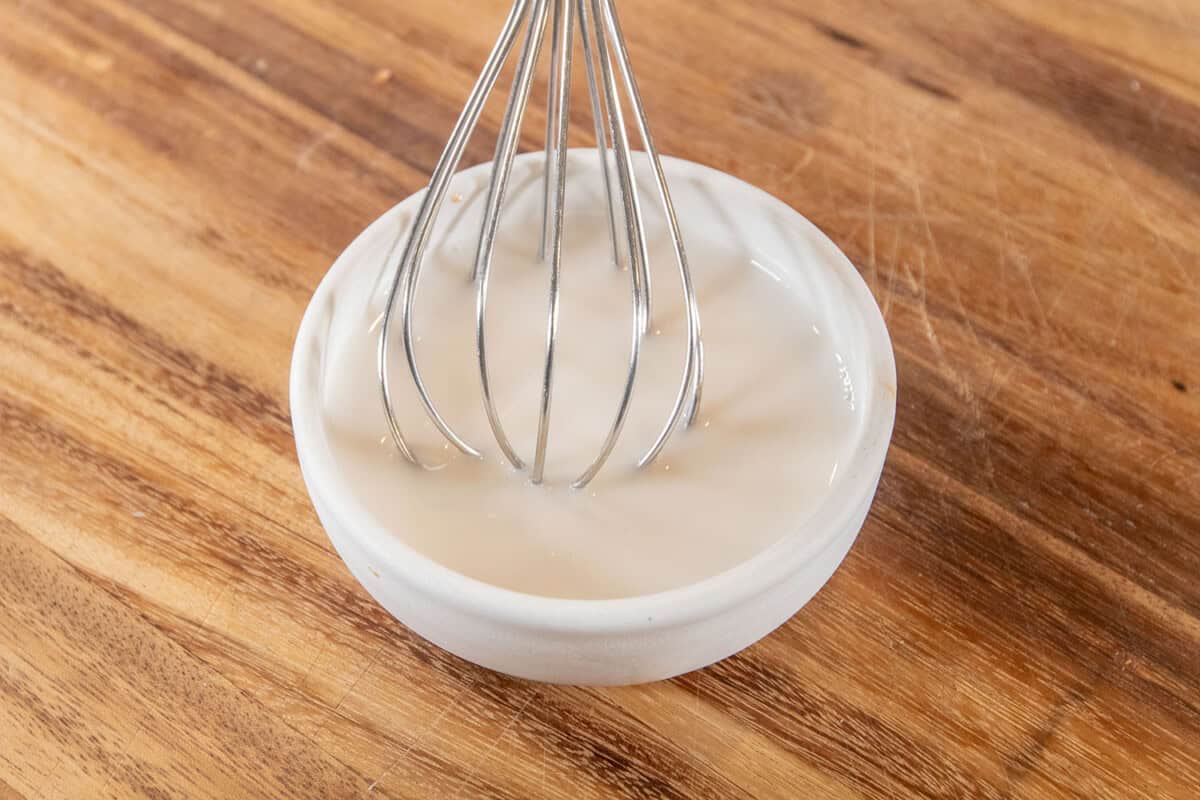 bowl of milk, maple syrup, and mustard with a whisk