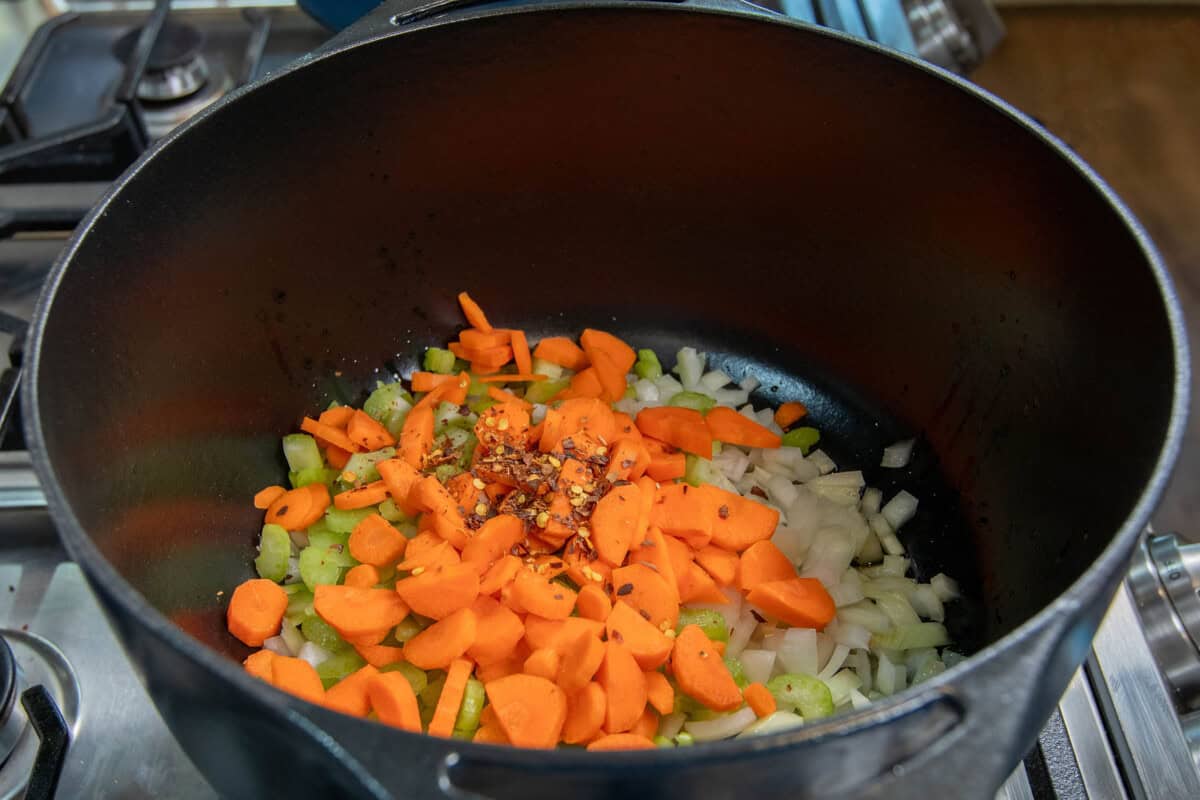 adding carrots, onions, celery, and red pepper flakes to the pot