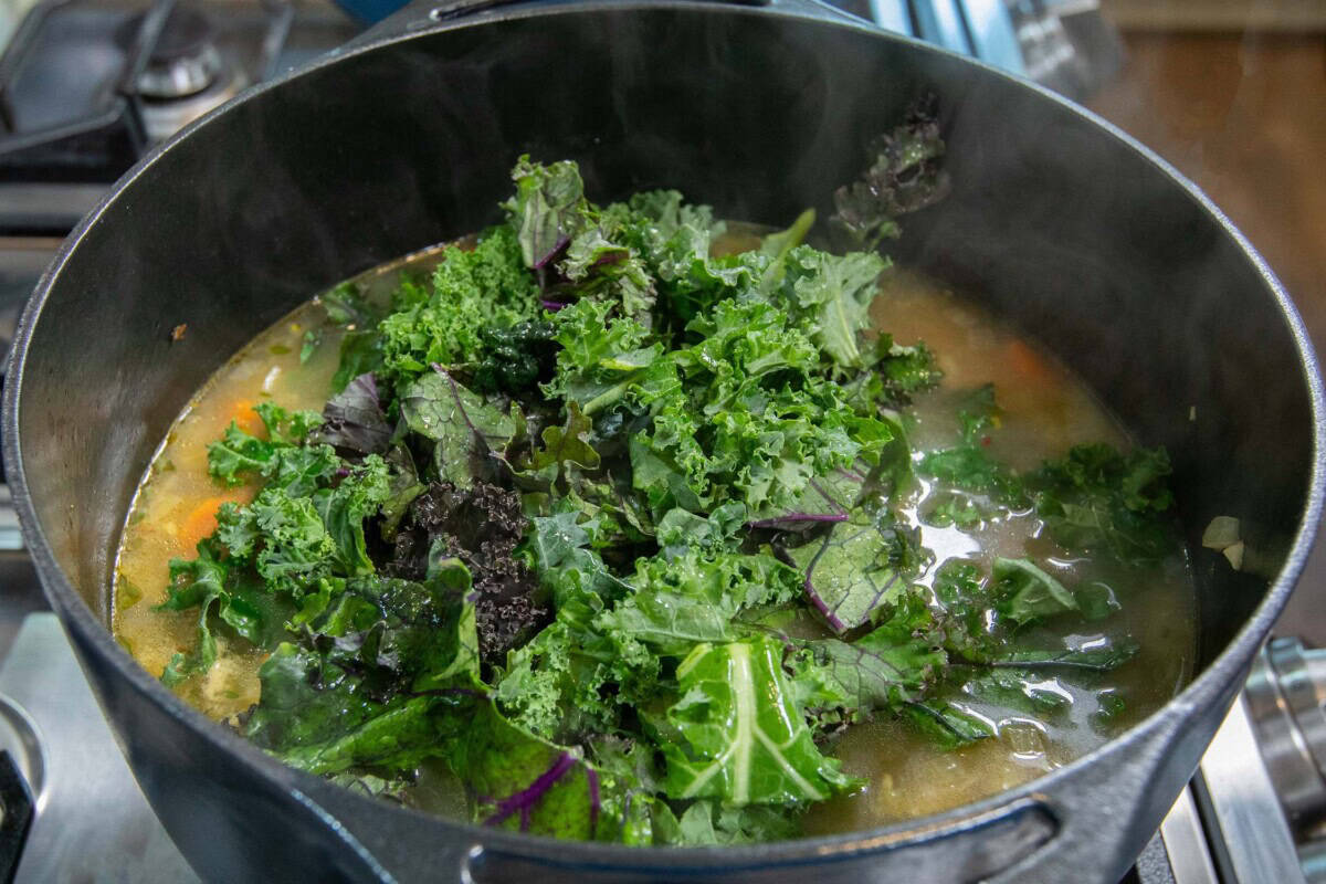 adding fresh kale to the pot of soup