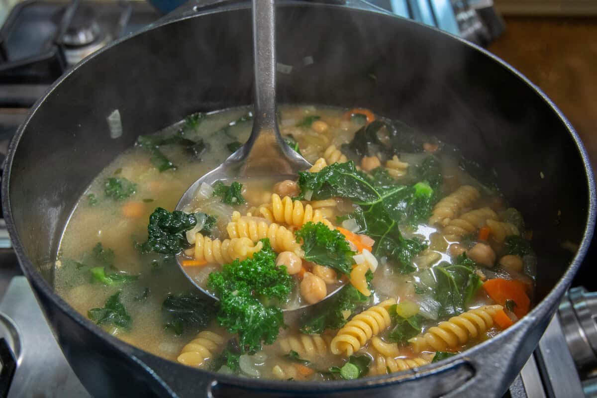 scooping chickpea noodle soup out of pot with a ladle