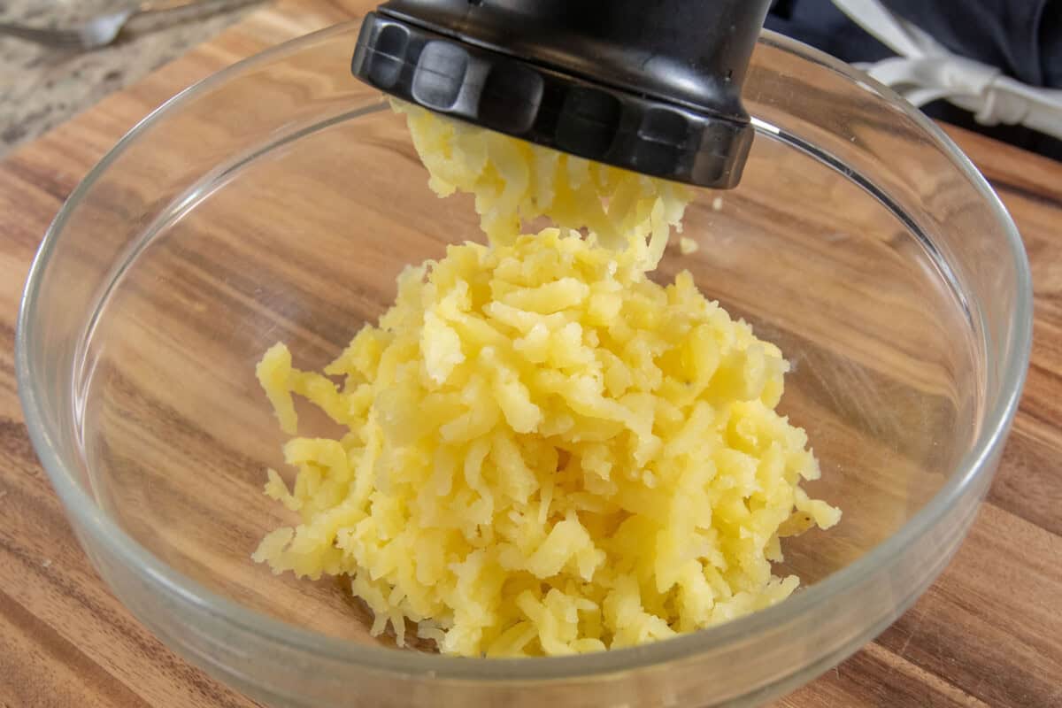 ricing cooked potatoes into glass bowl