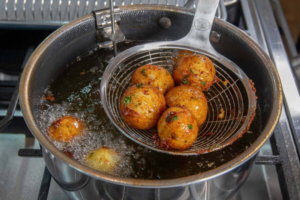 metal slotted spoon scooping crispy fried potato balls out of hot oil