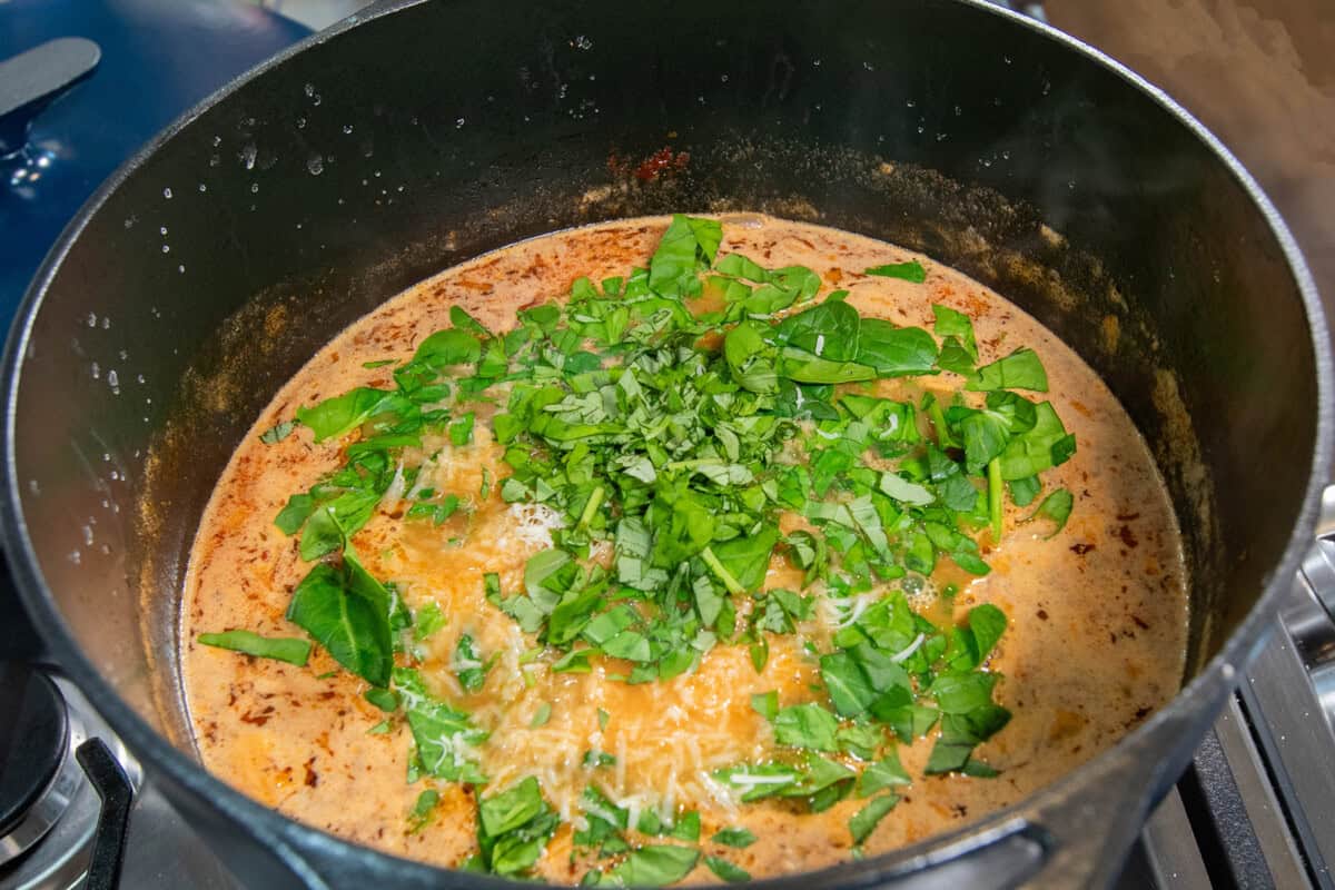 adding fresh spinach to the pot of soup